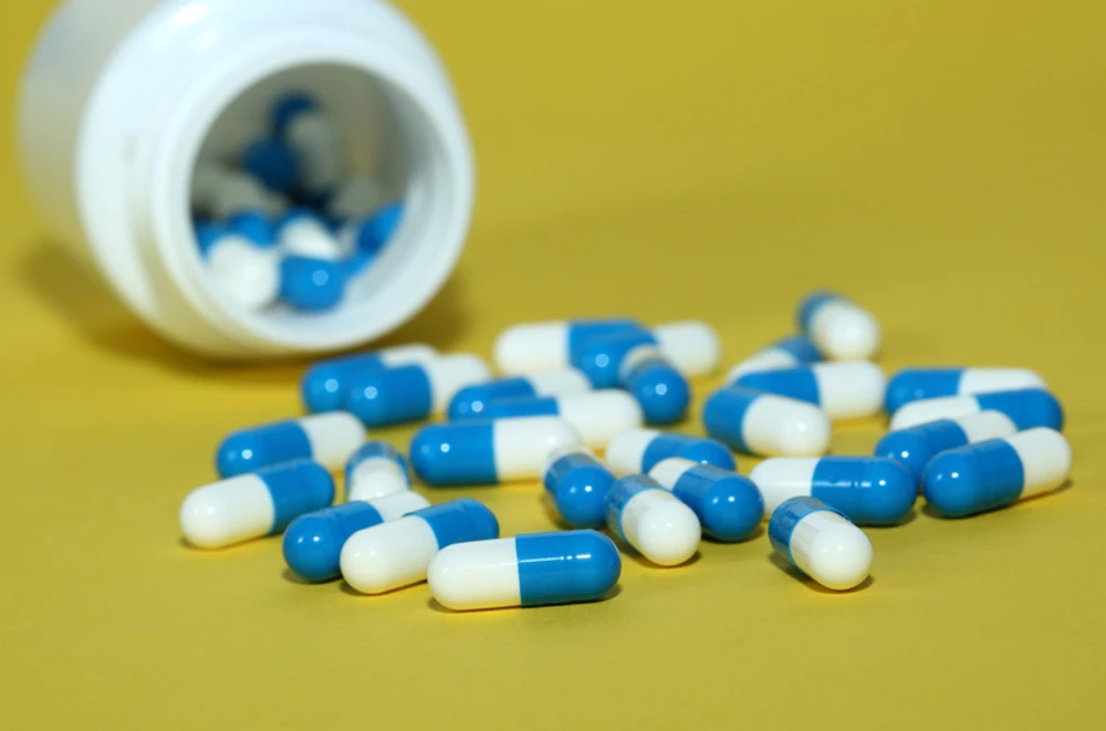 blue and white capsules spilling from pill bottle